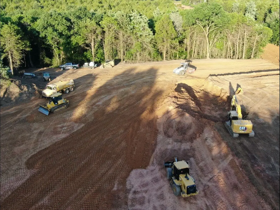 Aerial view of dozers and graders shaping a large building pad cut out of Oklahoma woods