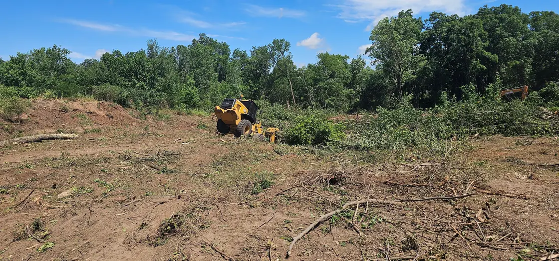Skid steer clearing the last brush from a cleared lot under blue Oklahoma sky