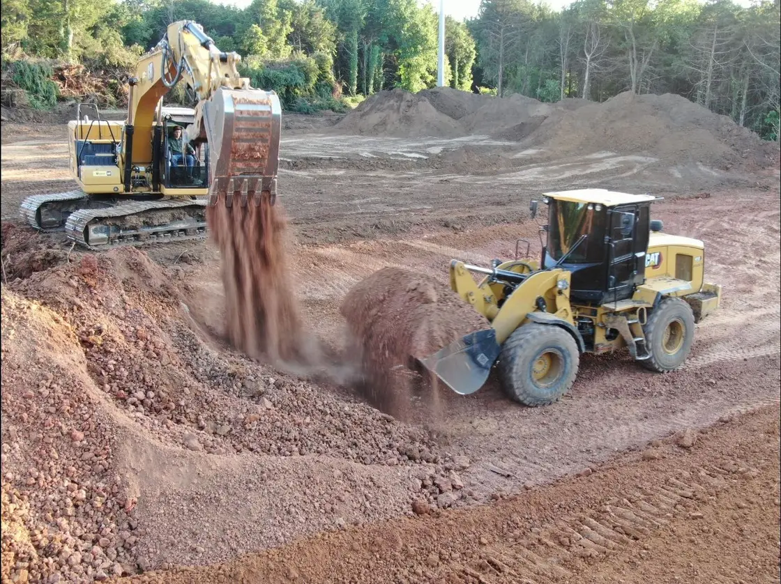 Excavator dumping a bucket of dirt while a wheel loader shapes the cut on an Oklahoma excavation job