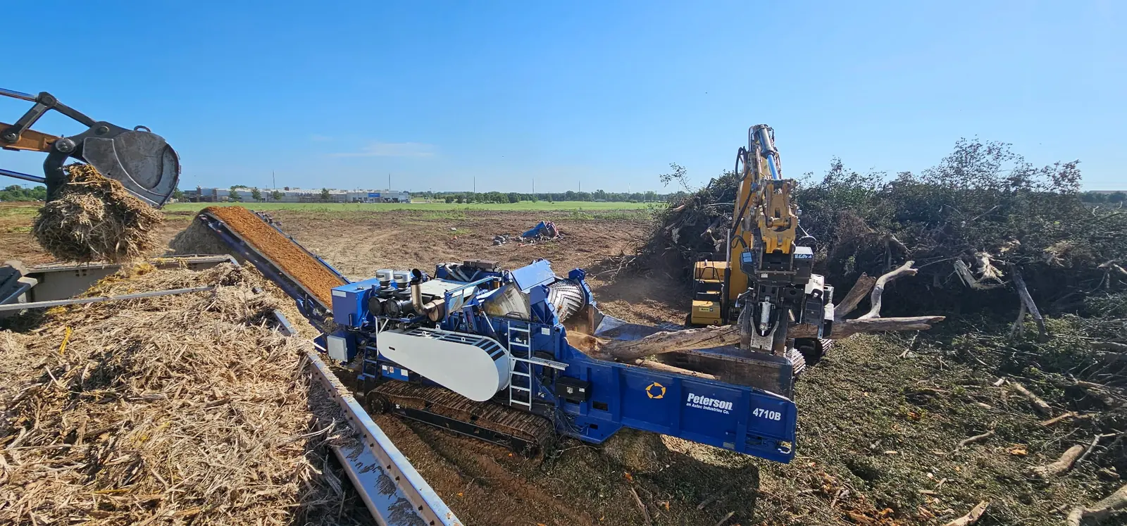 Peterson 4710B horizontal grinder fed by an excavator, turning cleared brush into wood chips on an Oklahoma job